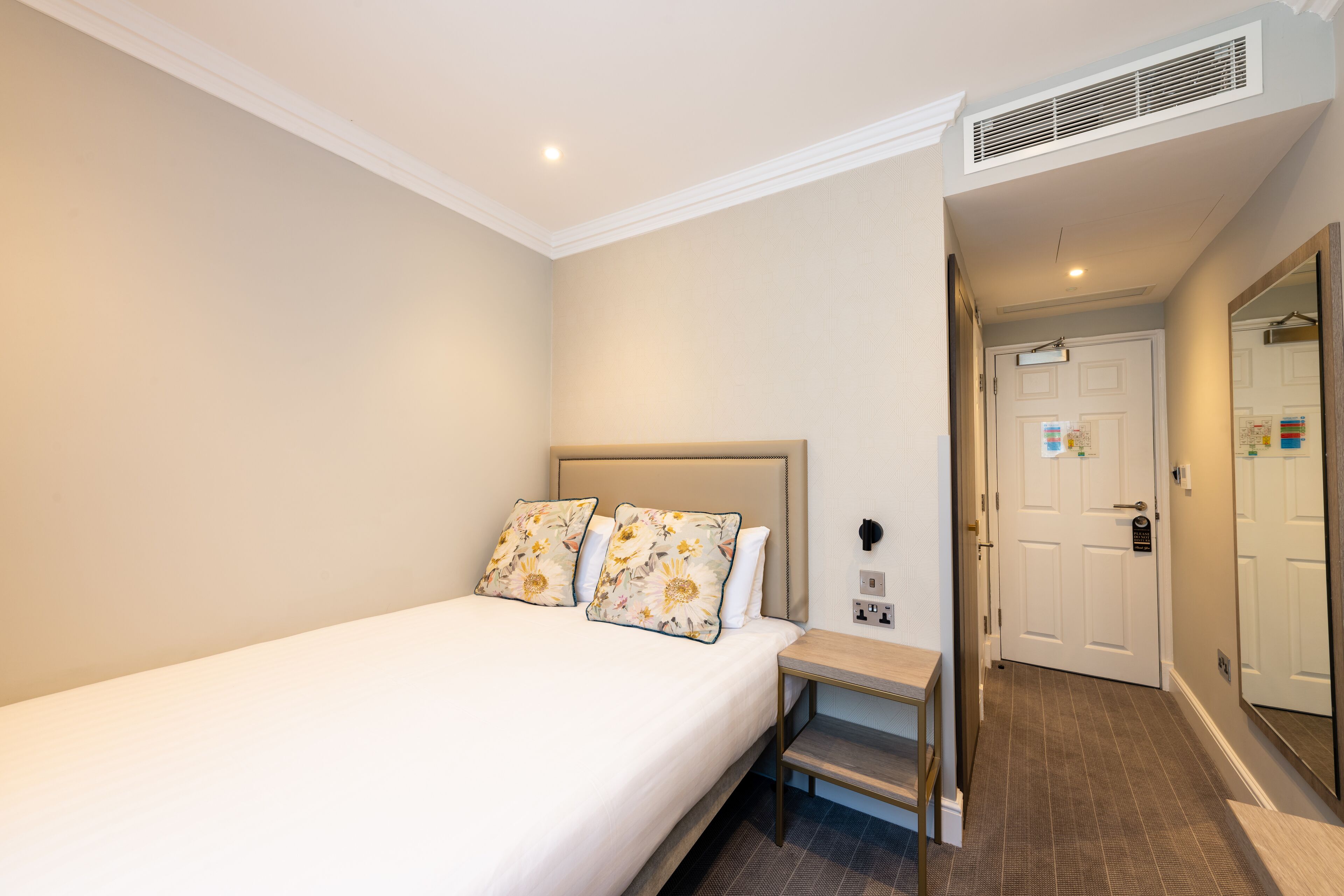 Un dormitorio con una cama, una mesita de noche, una puerta y un pasillo.