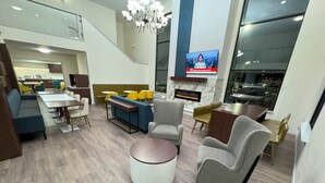 A modern hotel lobby with a dining area, seating, a fireplace, and a TV displaying news. - Comfort Inn & Suites Salt Lake City I-80 I-15 Downtown (Salt Lake City)