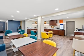 Una habitación de hotel moderna con kitchenette, un comedor con mesas y sillas, y una sala de estar independiente con sofá.