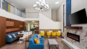 A modern hotel lobby with a blue sofa, yellow chairs, a fireplace, and a TV mounted on the wall. - Comfort Inn & Suites Salt Lake City I-80 I-15 Downtown (Salt Lake City)
