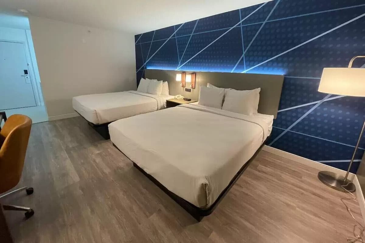 A hotel room with two beds, a desk, a chair, and a wall with a geometric pattern.