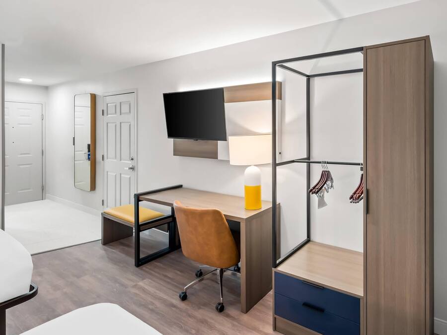 A modern bedroom with a desk, chair, bed, wardrobe, and TV.