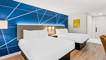 Habitación de hotel con dos camas, un muro azul con diseño, piso de madera y una puerta.