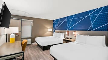 Quarto de hotel com duas camas, uma mesa, uma cadeira, uma televisão e uma parede com padrão geométrico.