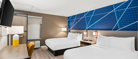 A hotel room with two beds, a desk, a chair, a TV, and a wall with a geometric pattern.