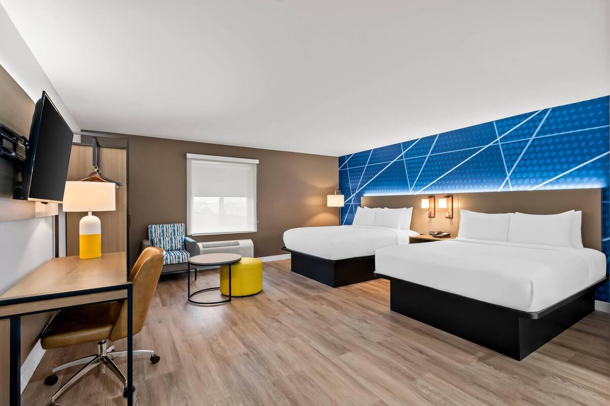A hotel room with a bed, two bedside tables, a desk with a chair, a small table with a chair, and a TV.
