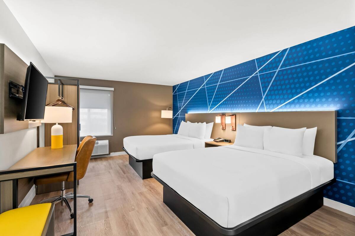 A hotel room with two beds, a desk with a chair, a TV, and a window.