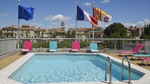 A swimming pool with lounge chairs and flags of the European Union and Spain. - Mercure Arles Centre Arenes (Arles)