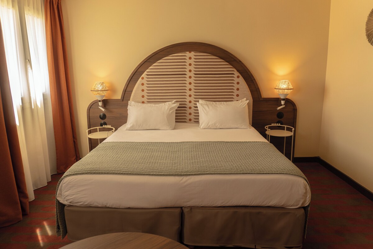 Habitación de hotel con una cama grande, dos lámparas de noche y una ventana con cortinas.