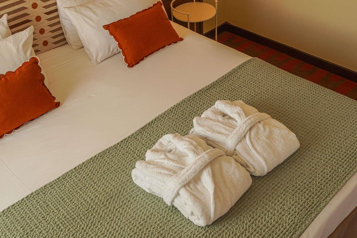 A neatly made bed with white linens, two brown pillows, and a green textured blanket.