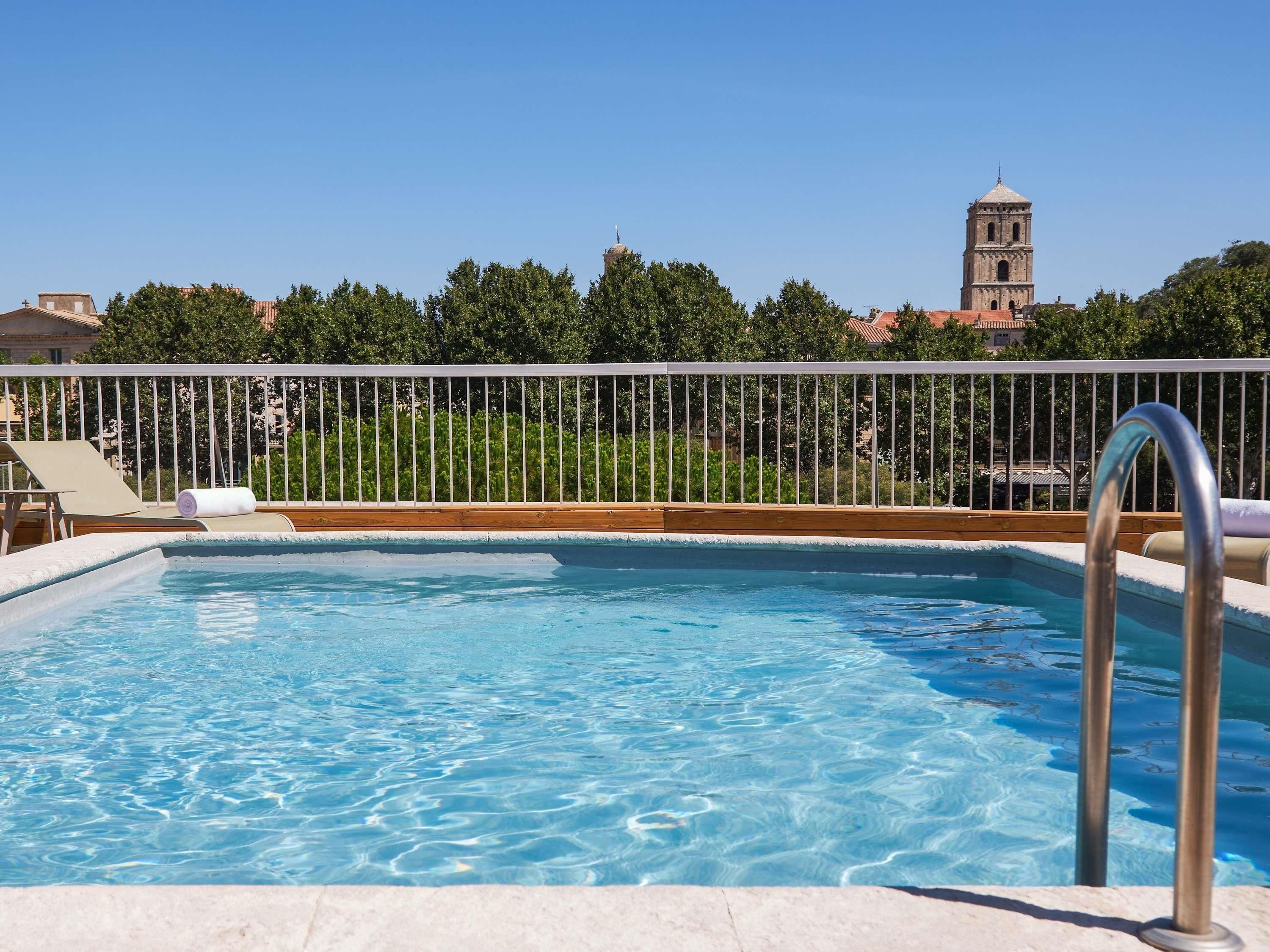 A swimming pool with a metal ladder, lounge chairs, and a view of a tower in the background.