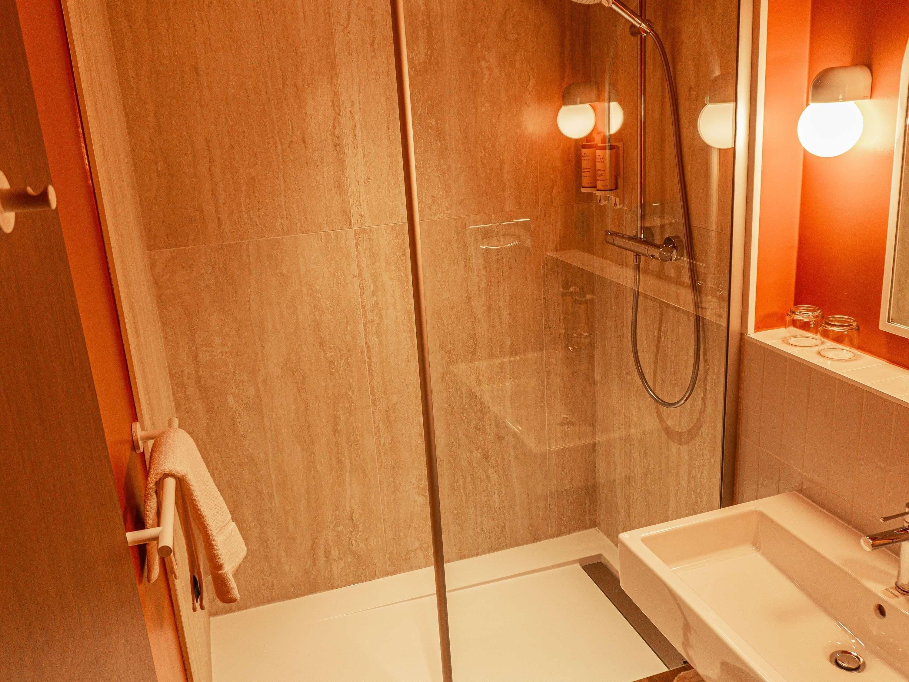 A bathroom with a glass-enclosed shower, a white sink, and a mirror with wall-mounted lights.