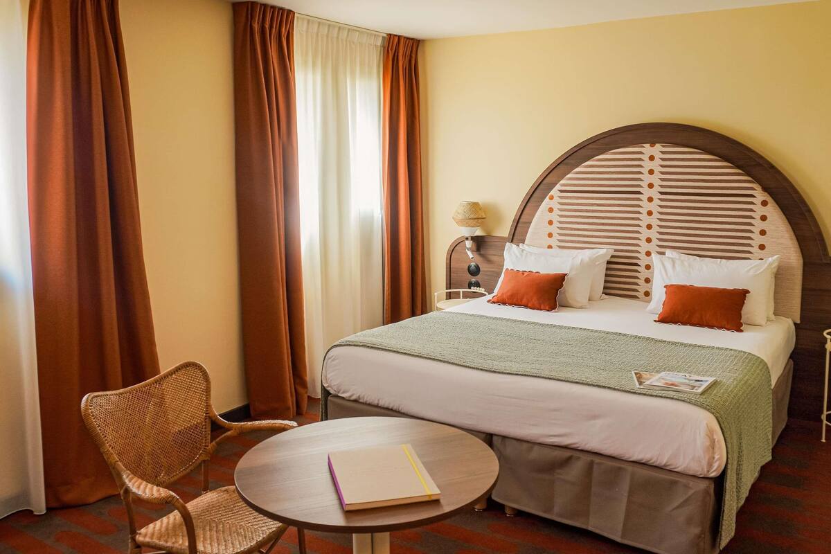 A hotel room with a bed, a round table, a chair, and a lamp.
