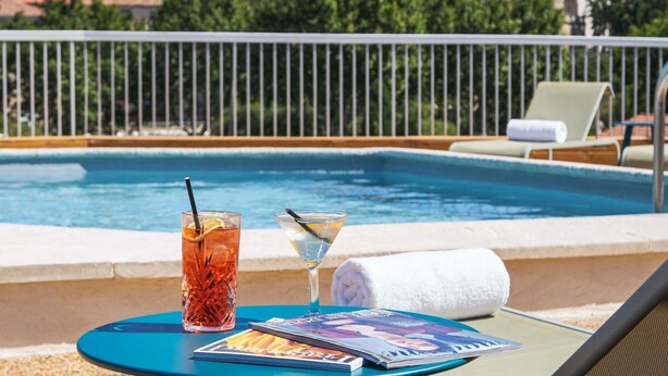 A poolside setting with a drink, a magazine, and a towel on a table.