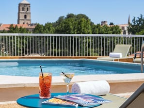 A poolside setting with a drink, a magazine, and a towel on a table. - Mercure Arles Centre Arenes (Arles)