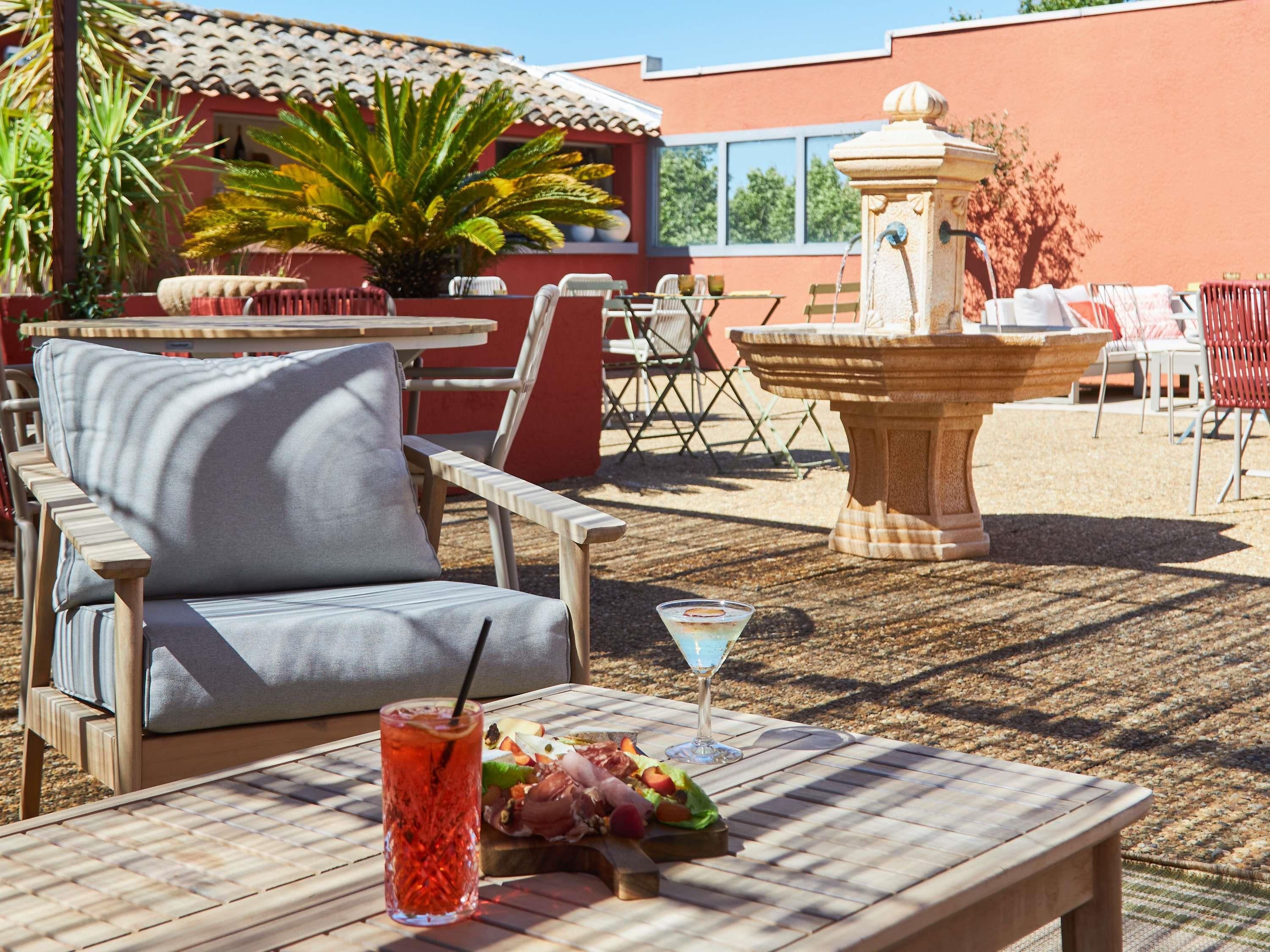 Un espace extérieur aménagé avec une table, des chaises, une boisson et une petite fontaine.