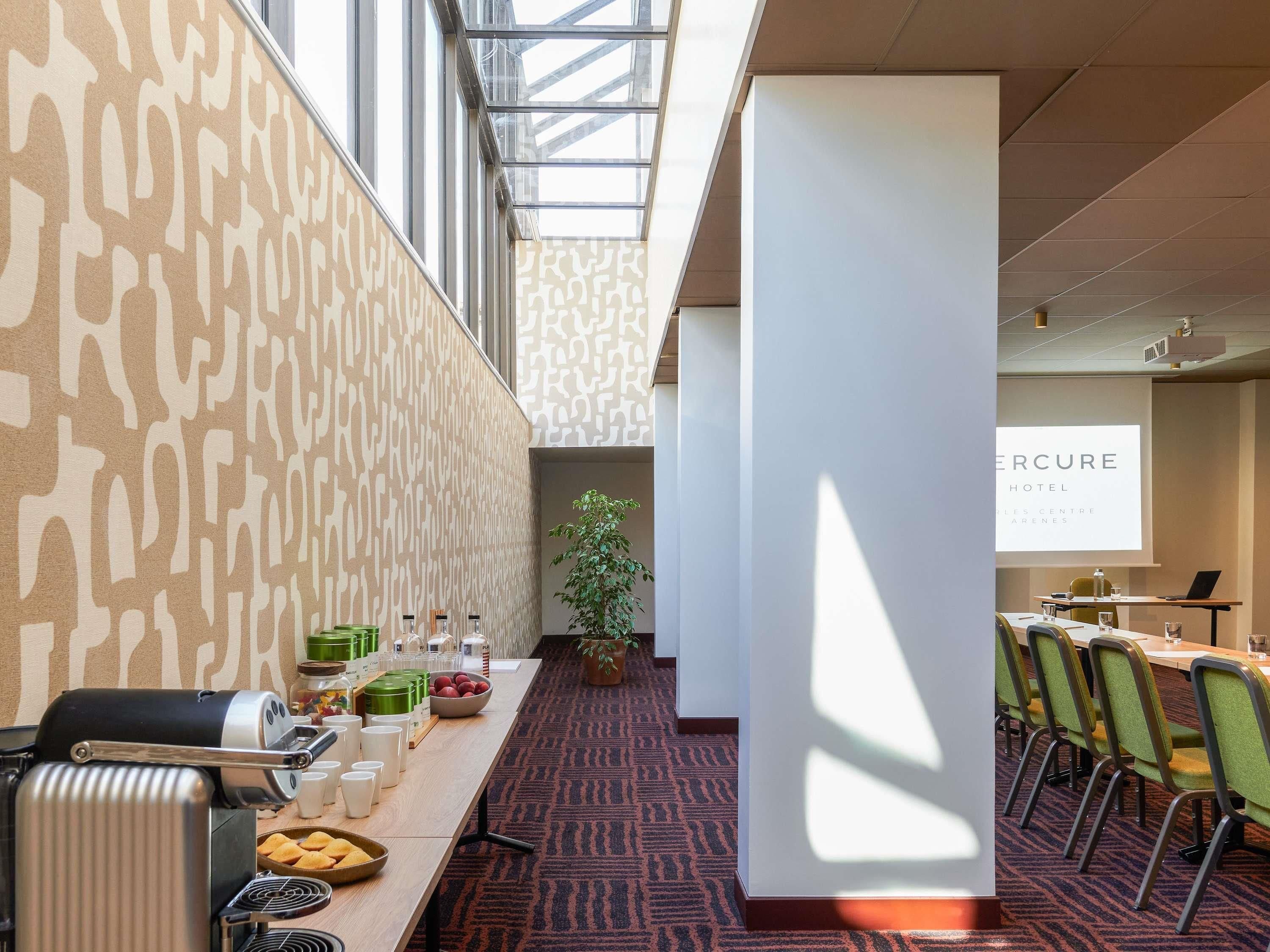 Ein Konferenzraum mit langem Tisch, Stühlen, einem Grill und einer Projektionsleinwand, auf der 'ERCURE HOTEL' angezeigt wird.