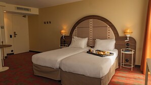 A hotel room with a large bed, two bedside tables with lamps, a small table, and a door. - Mercure Arles Centre Arenes (Arles)
