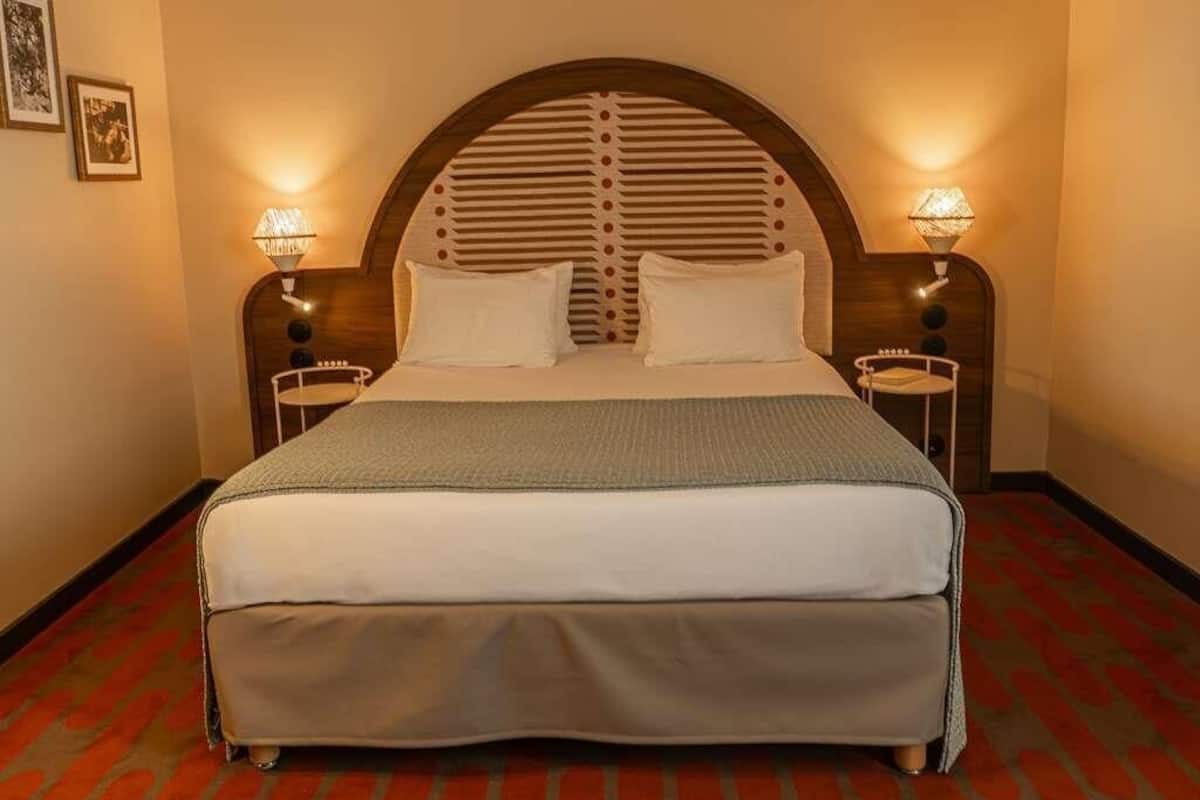 A hotel room with a large bed, two bedside lamps, and a patterned carpet.