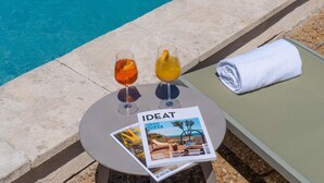 A poolside setting with two drinks on a table, a magazine, and a towel on a lounge chair. - Mercure Arles Centre Arenes (Arles)