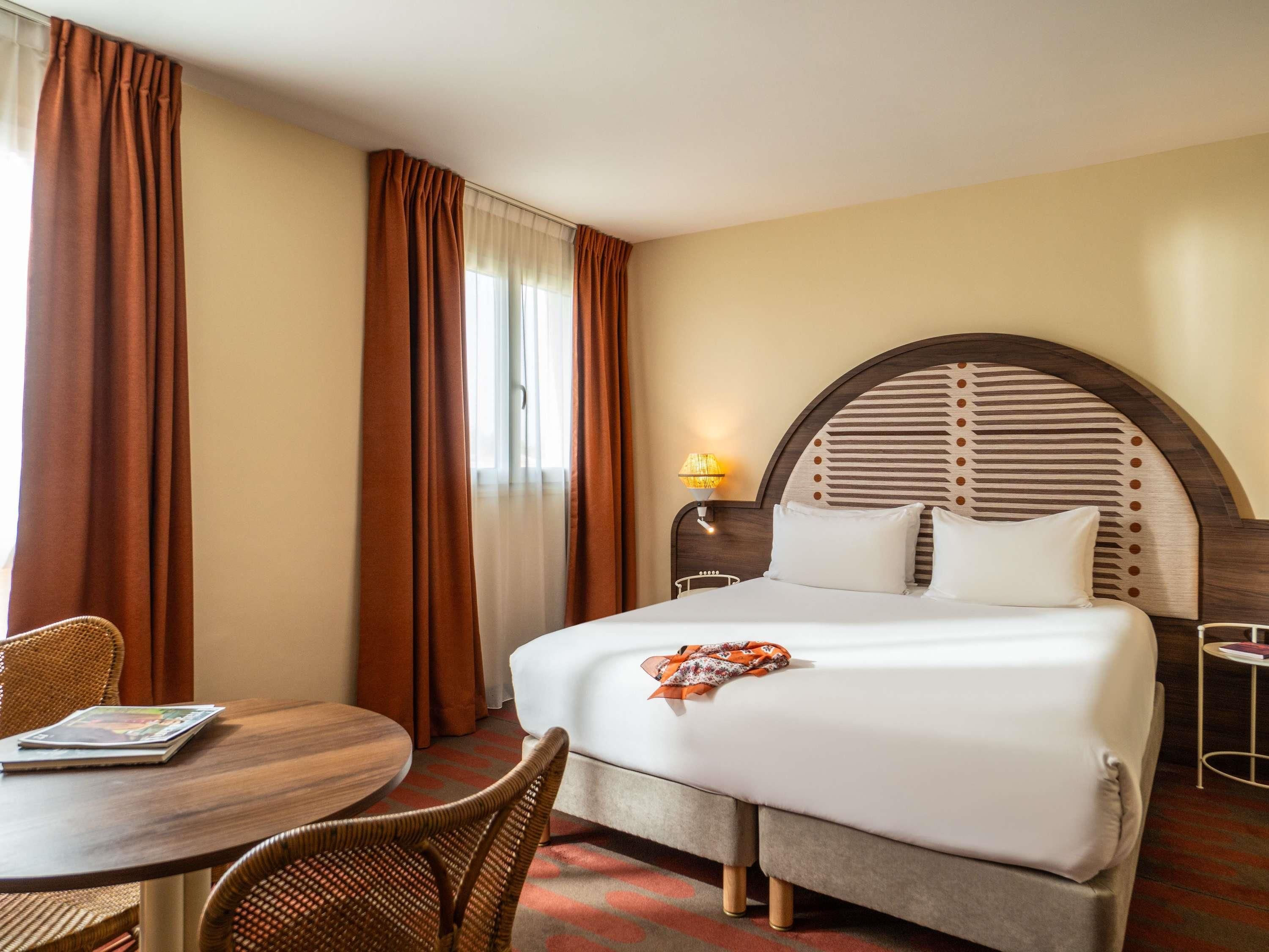 Une chambre d’hôtel avec un lit, une table ronde, une chaise et une lampe.