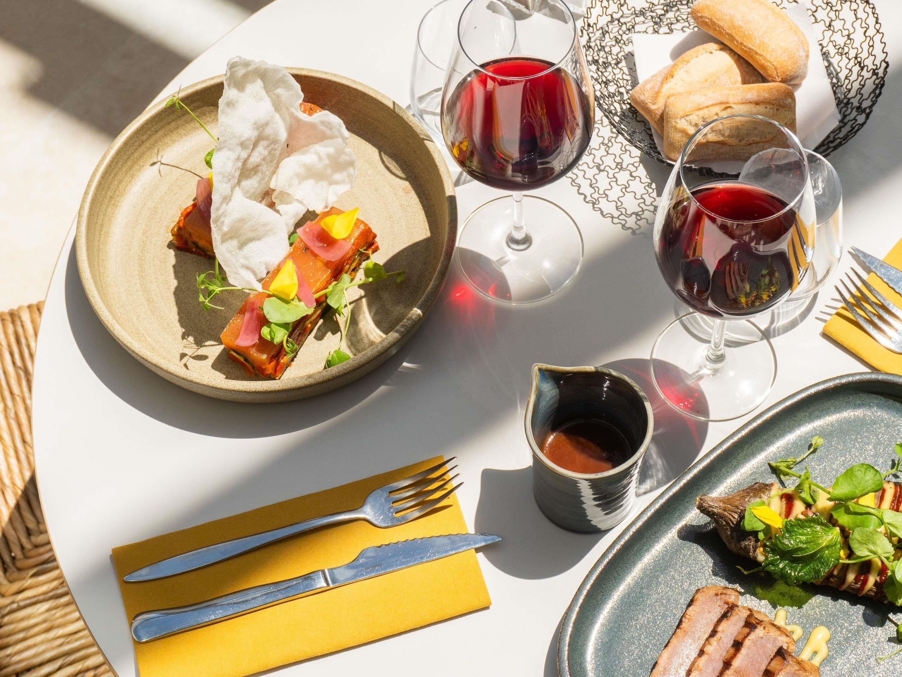 Una tavola imbandita con piatti di cibo, bicchieri di vino rosso e posate.