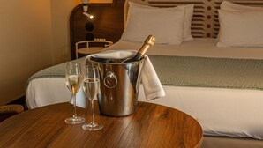 A hotel room with a bed, a bedside table with a champagne bottle and glasses, a lamp, and a patterned headboard. - Mercure Arles Centre Arenes (Arles)