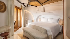 A modern bedroom with a large bed, a small seating area, and a view of the outdoors. - Cala di Volpe, a Luxury Collection Hotel, Costa Smeralda (Arzachena)