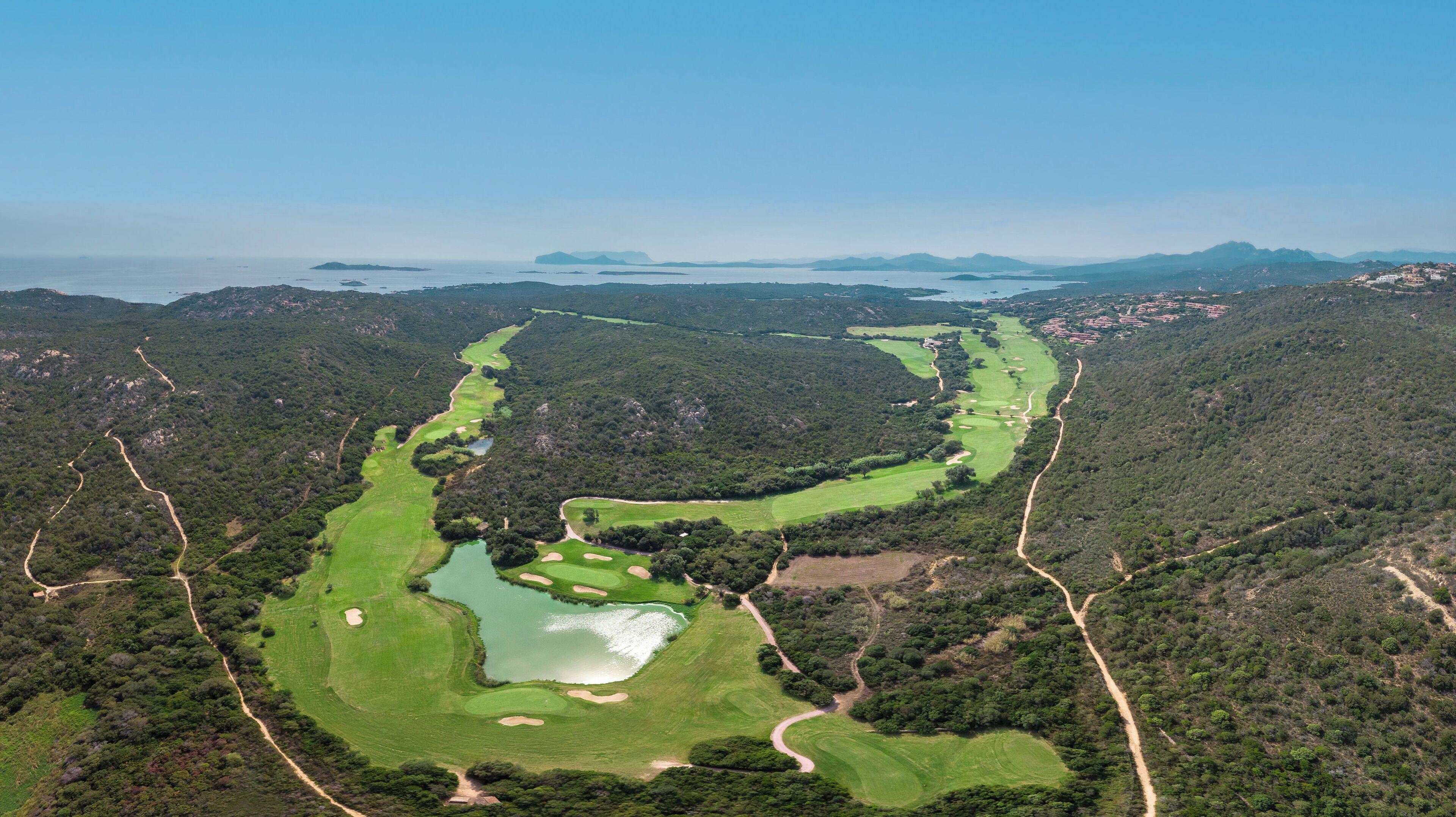 Vue aérienne d’un parcours de golf comportant plusieurs trous, entouré d’une forêt dense et de collines.