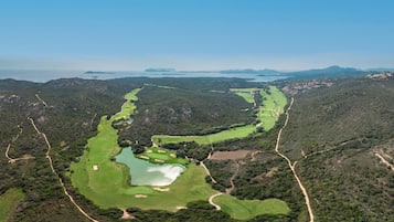 Vue aérienne d’un parcours de golf comportant plusieurs trous, entouré d’une forêt dense et de collines.