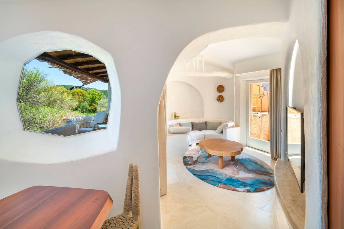 Un intérieur moderne donnant sur un espace verdoyant, avec une table en bois et un coin salon agrémenté d’un tapis à motifs.