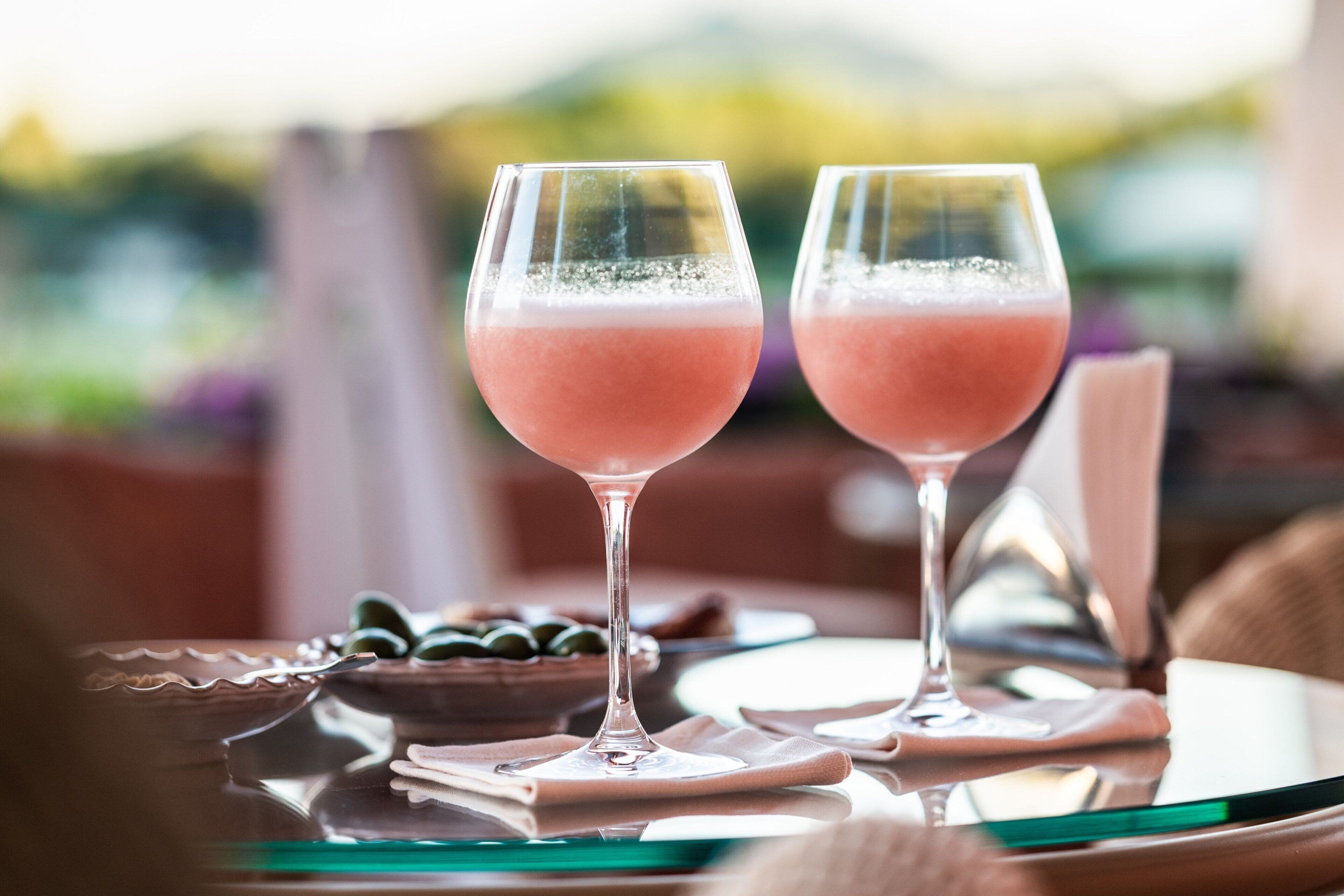 Dos vasos de bebida rosada sobre una mesa, con un fondo borroso al aire libre.