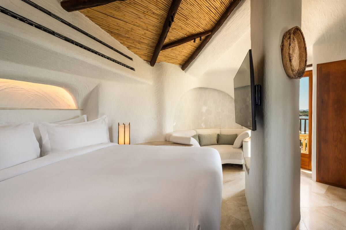 Une chambre moderne avec un grand lit, un canapé, un téléviseur à écran plat fixé au mur et un plafond en bois.