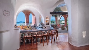 A bar area with a curved marble counter, wooden chairs, and a view of the sea through arches. - Cala di Volpe, a Luxury Collection Hotel, Costa Smeralda (Arzachena)