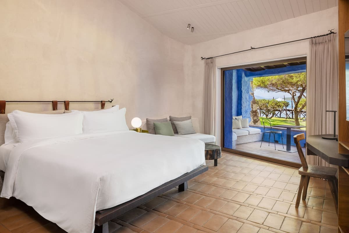 Une chambre dotée d’un grand lit, d’un bureau et donnant sur un patio avec coin salon extérieur.