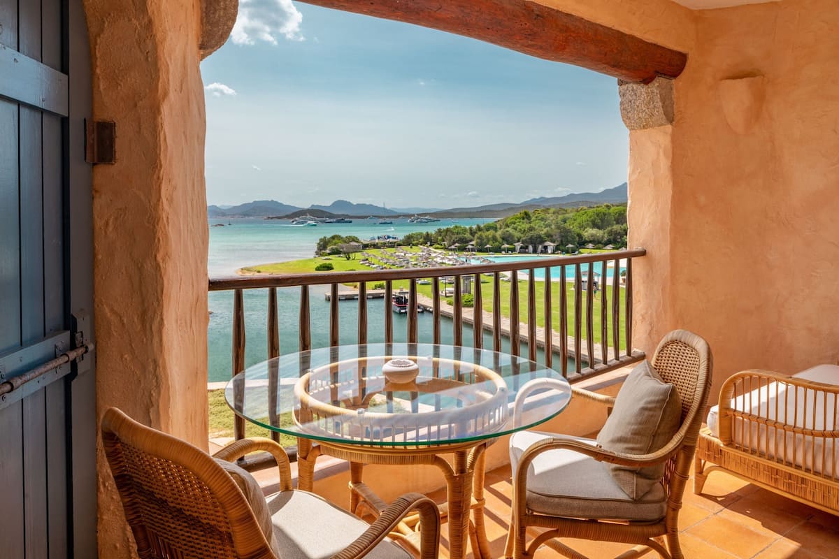 Un balcon agrémenté de meubles en osier, d’une table en verre et offrant une vue sur une plage et la mer.