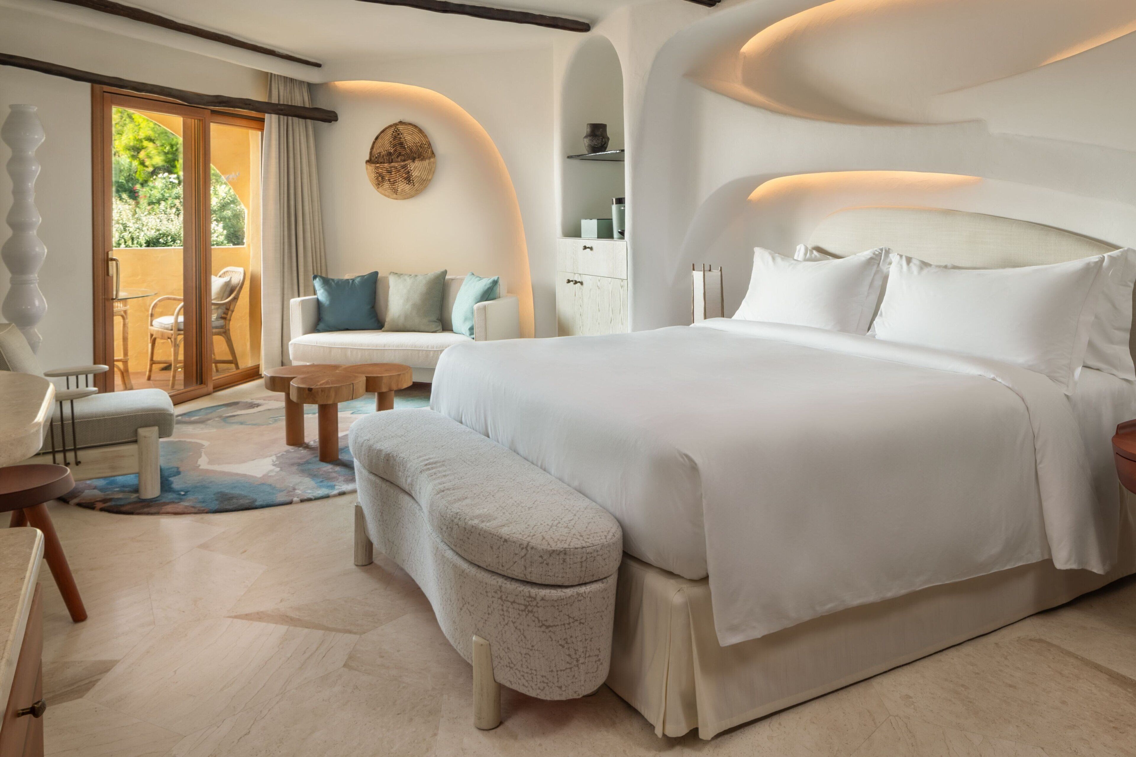 A modern bedroom with a large bed, a sofa, a small table, and a bench.