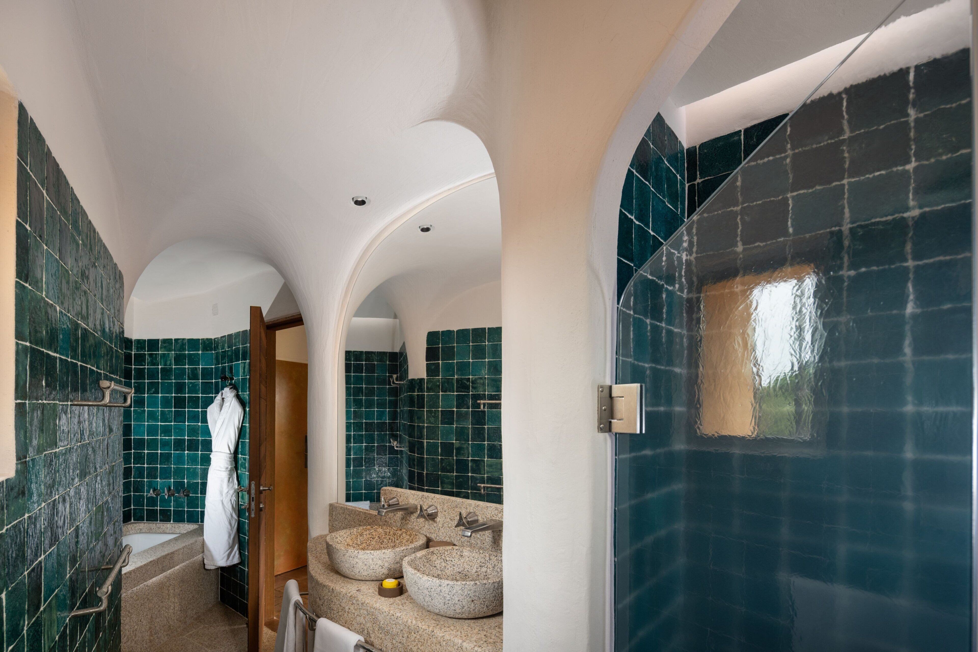 Un baño con una bañera blanca, dos lavamanos con lavabos de piedra redondos y un perchero para toallas.