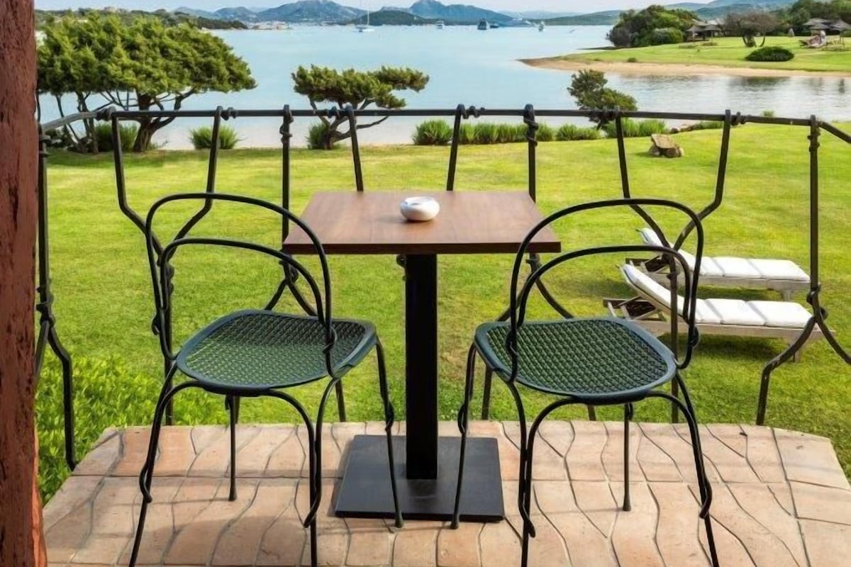 Una terraza con dos sillas y una mesa, con vistas a un lago y vegetación.