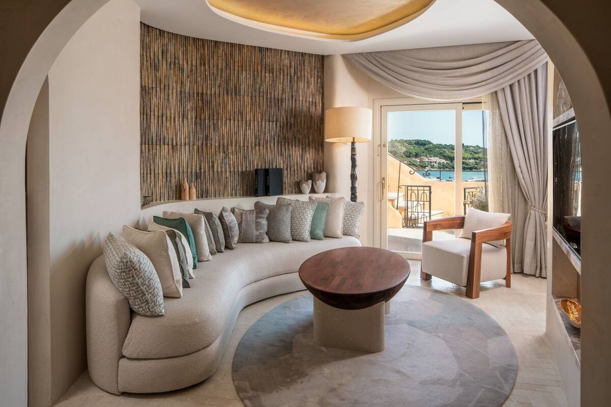 Un salon moderne avec un canapé aux lignes courbes, une table basse ronde et une vue sur un balcon avec une piscine.