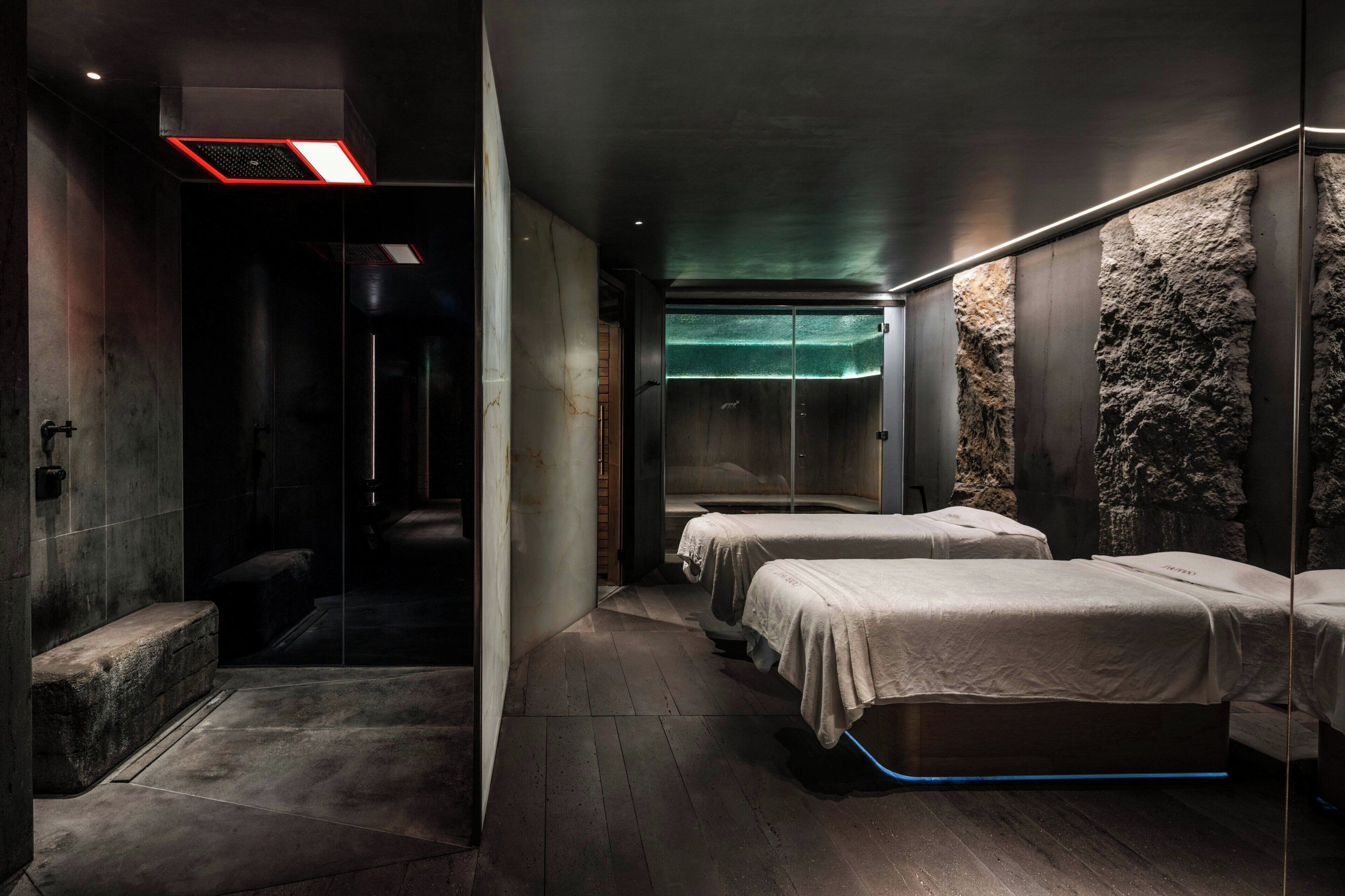 Habitación de hotel moderna con una pared de acento de piedra, cabina de ducha de vidrio y una cama con luz azul debajo del colchón.