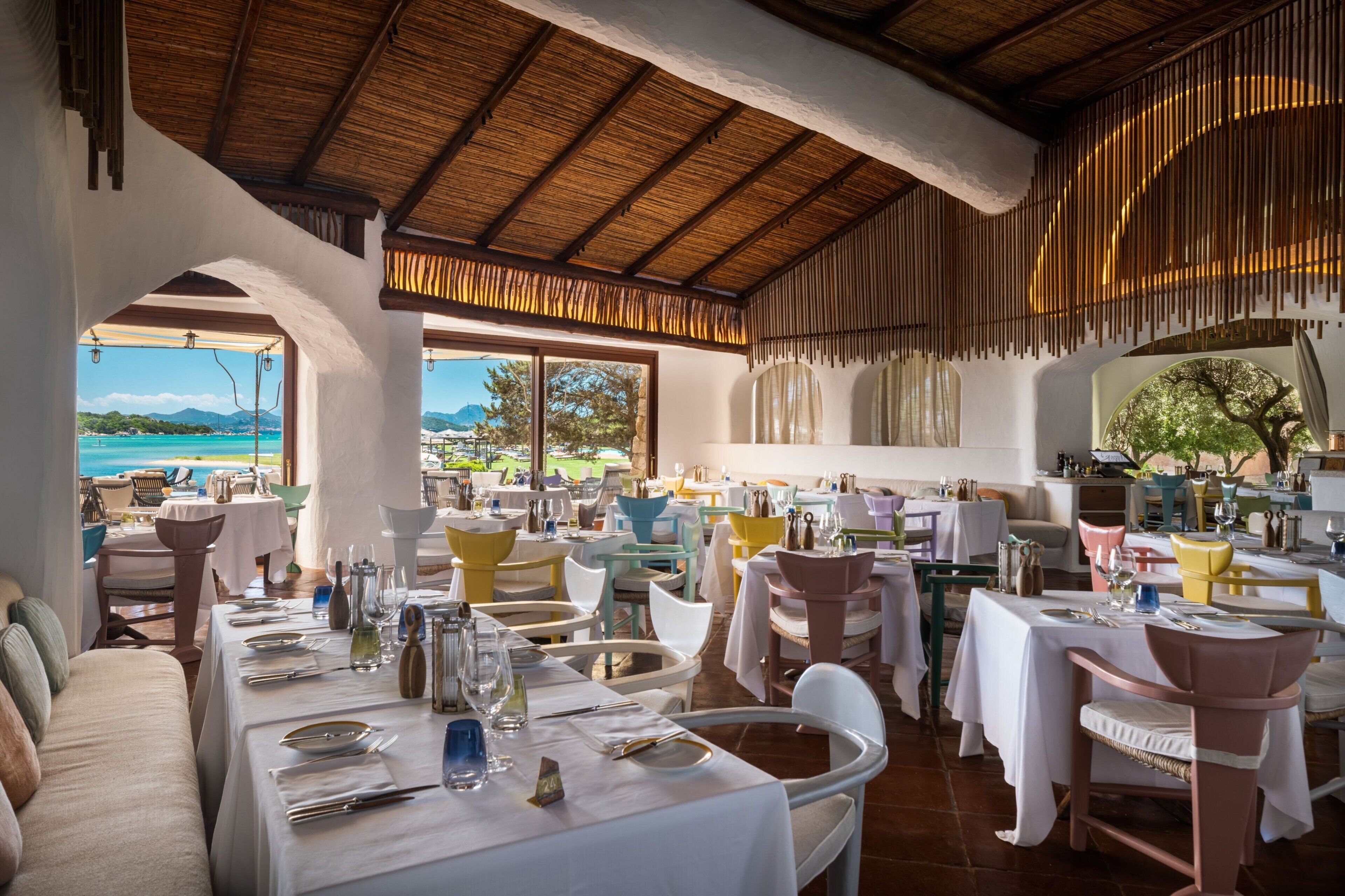 Un restaurant doté d’une terrasse offrant une vue sur la côte. Les tables sont dressées avec des nappes blanches et accueillent différents plats.