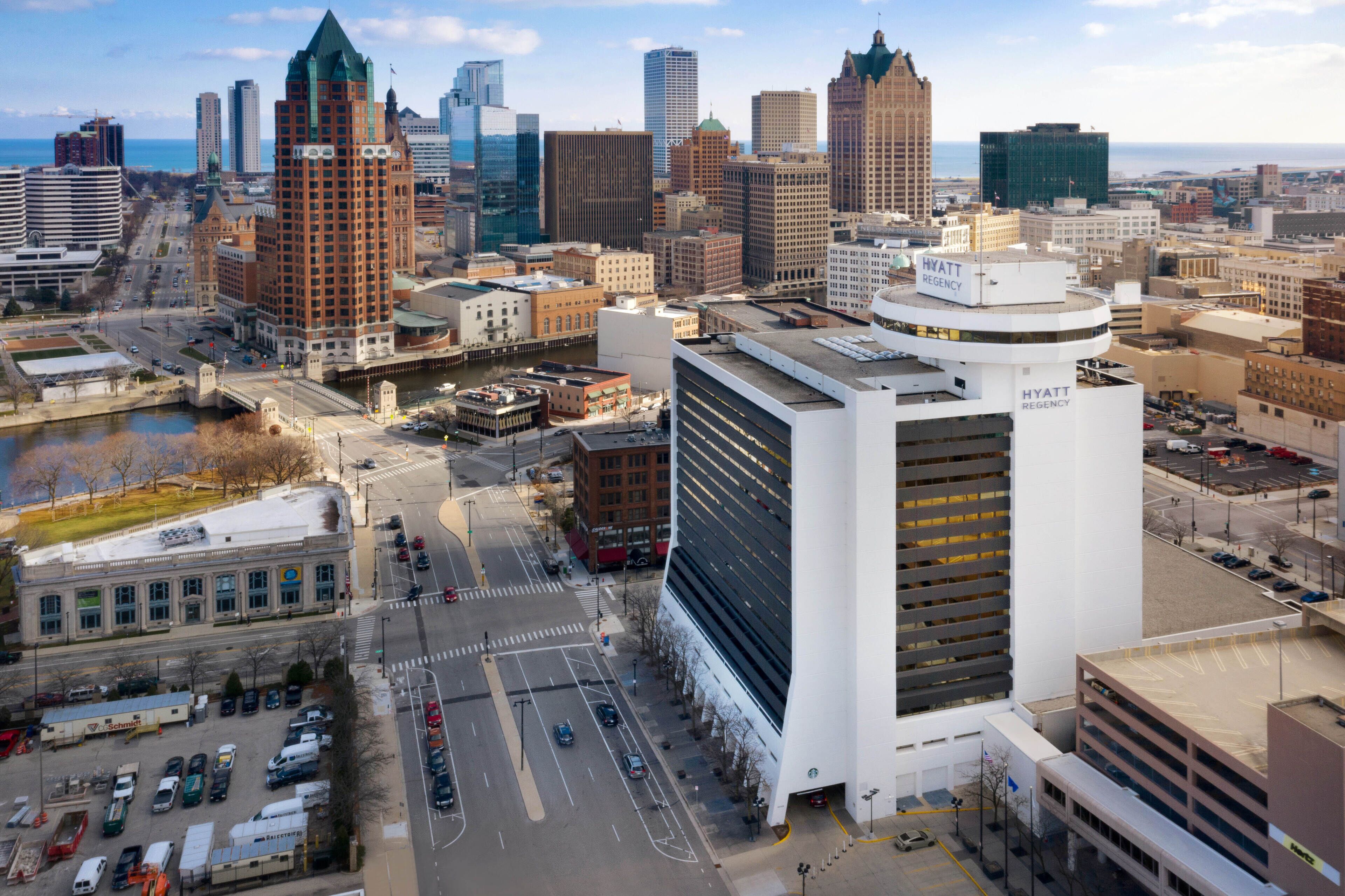 A modern hotel with a prominent glass facade, located in a downtown area with a view of the city skyline.