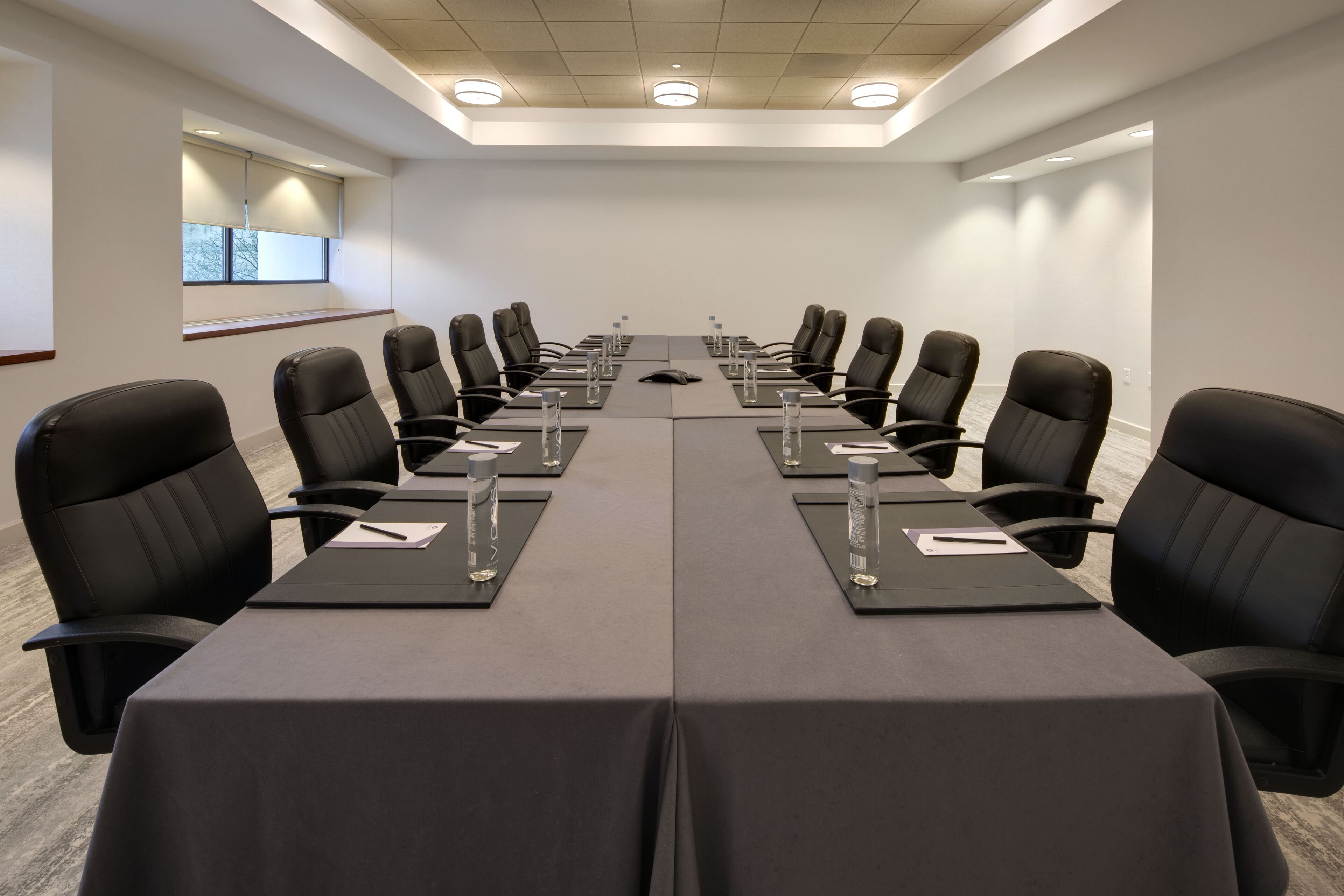 Un salón de conferencias con una larga mesa, sillas negras y botellas de agua.