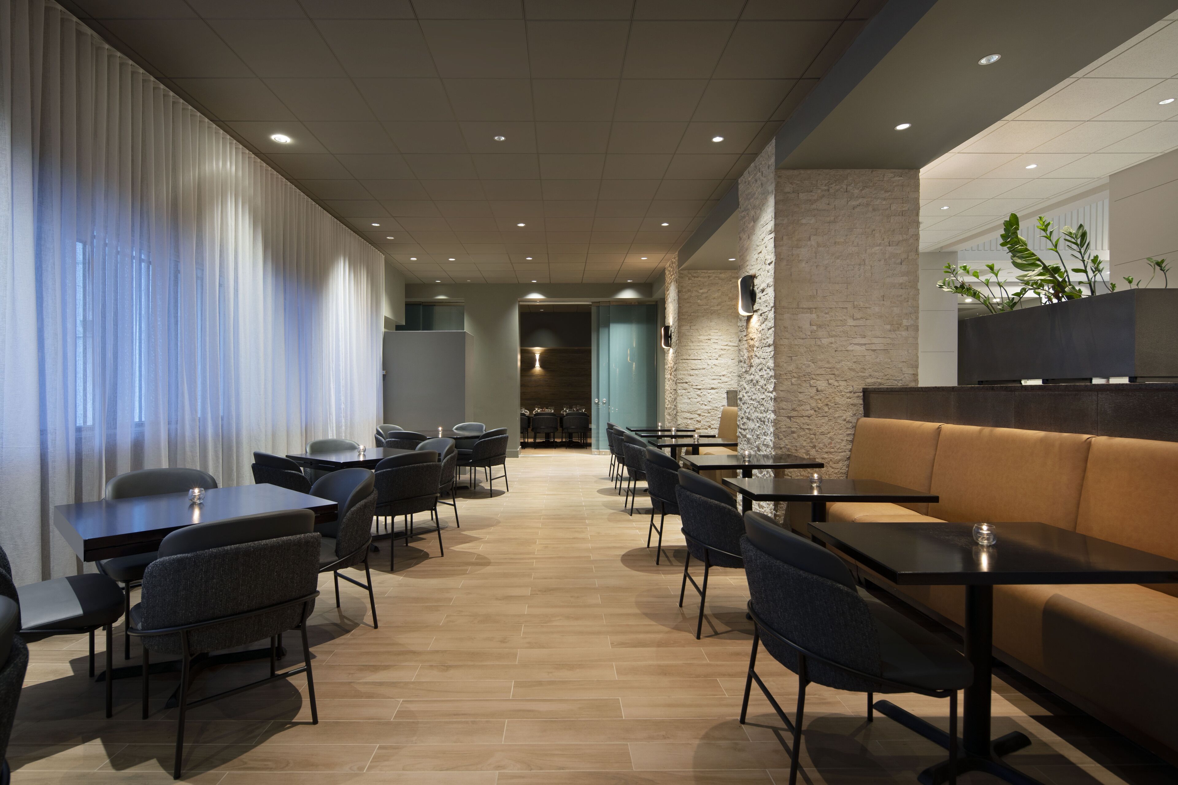 A modern hotel lobby with a long corridor, seating areas, and a stone accent wall.