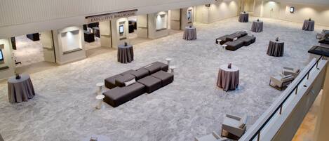Un hall d’hôtel spacieux, doté d’un plafond haut, de plusieurs espaces aménagés pour s’asseoir et d’un panneau indiquant l’emplacement d’une salle de réception de prestige.