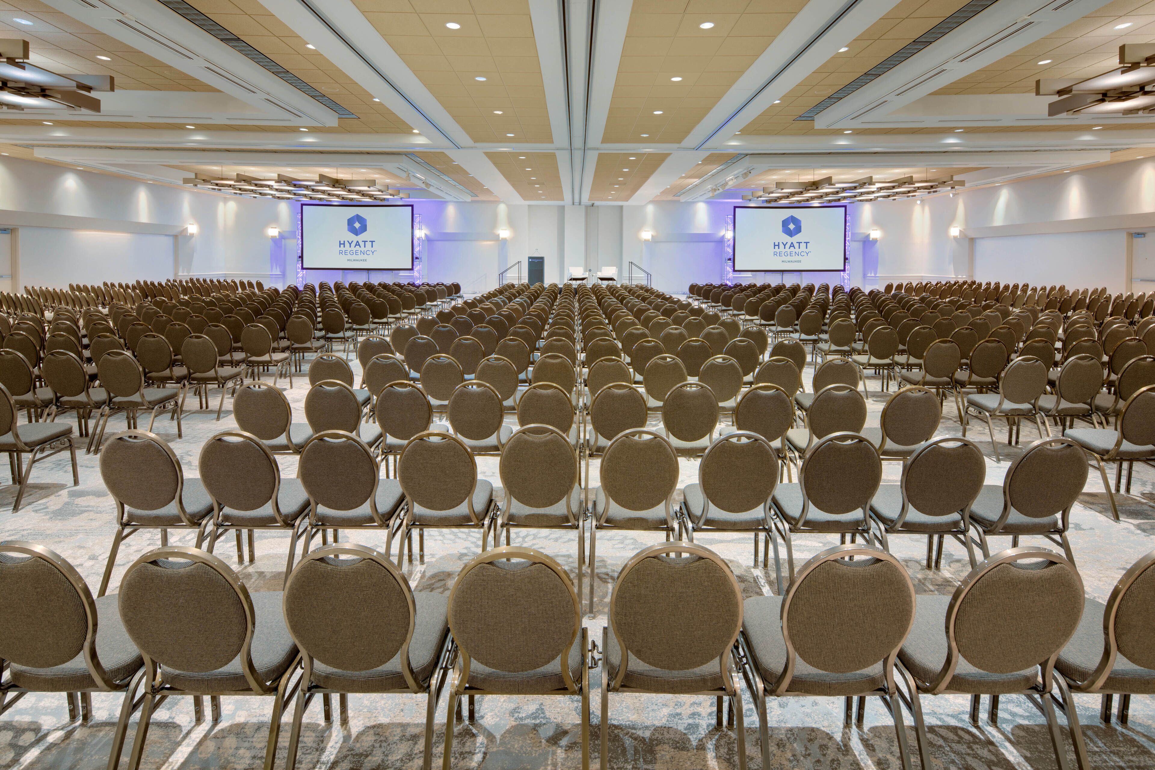 A large conference room with rows of chairs and two screens displaying the Hyatt Regency logo.