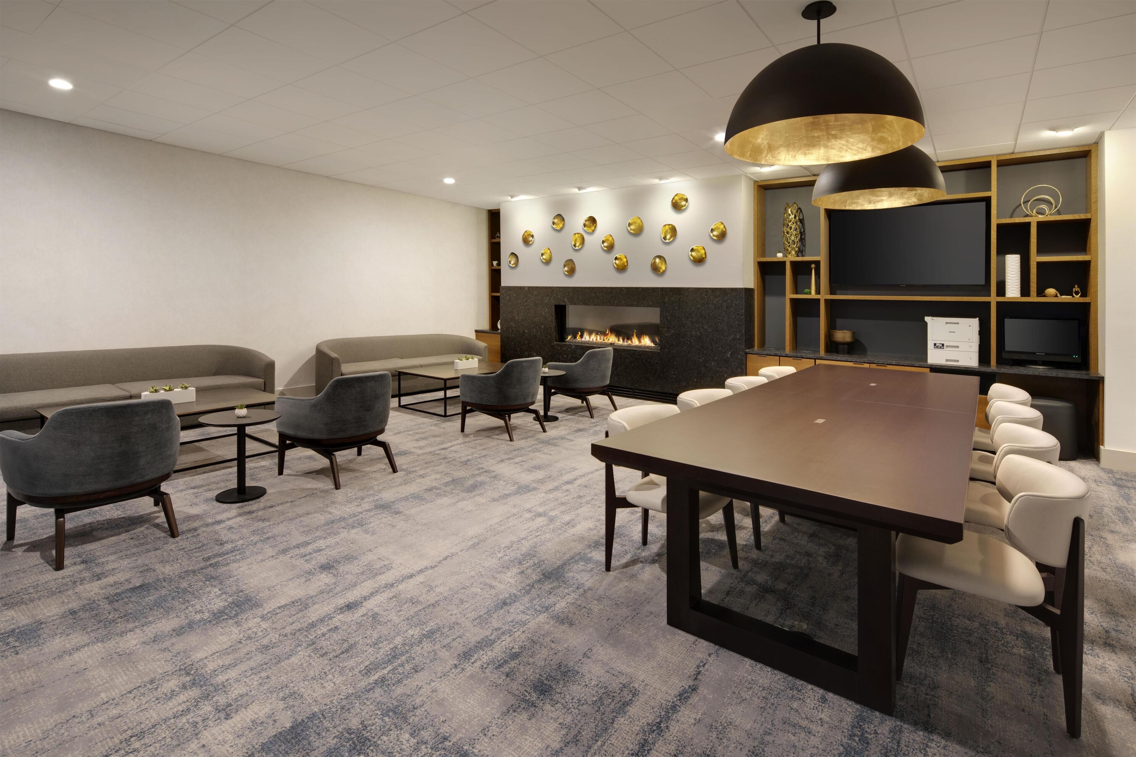 A modern meeting room with a large table, several chairs, a sofa, a fireplace, and a television.