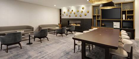 A modern meeting room with a large table, several chairs, a sofa, a fireplace, and a television.