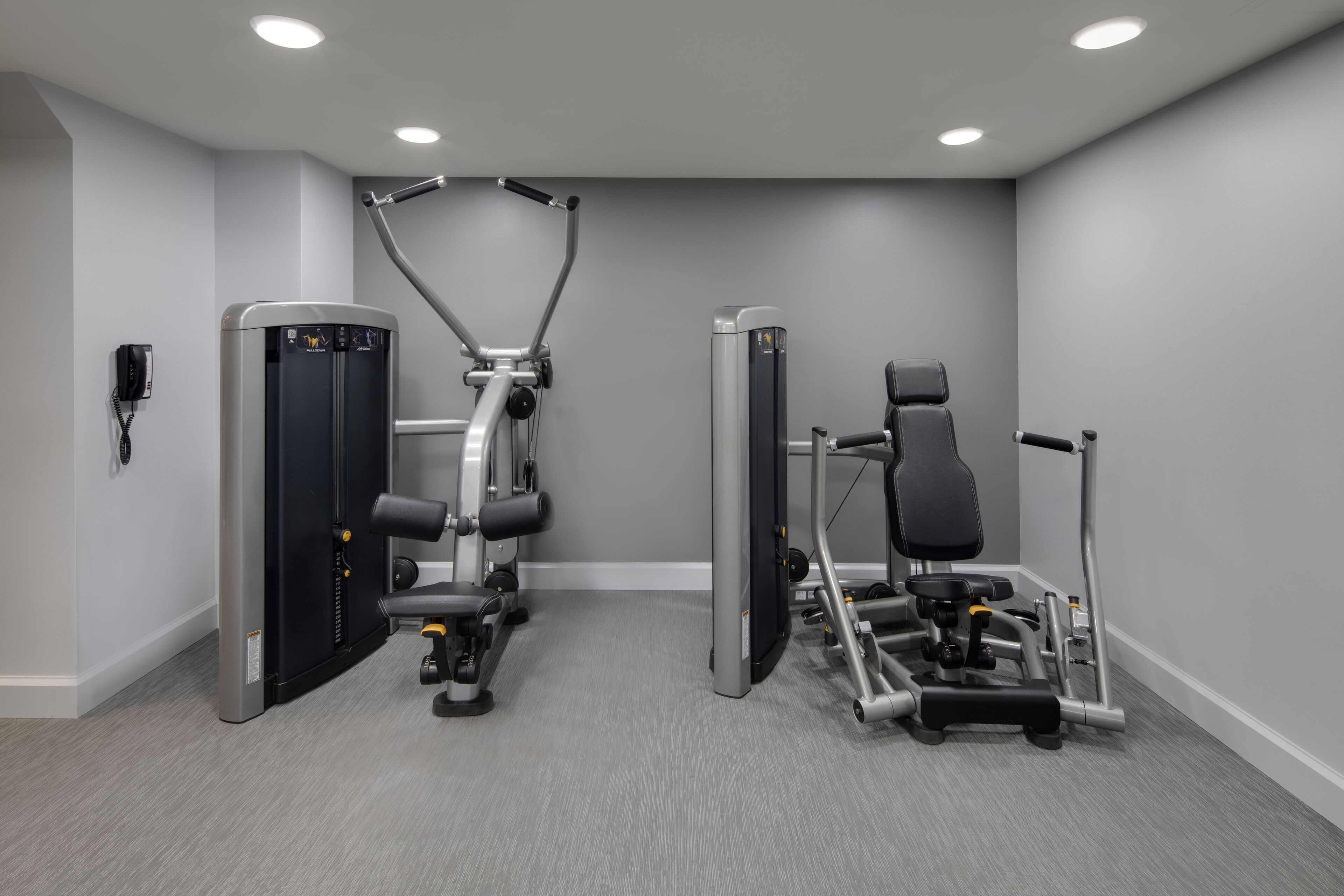 A modern gym with cardio machines and free weights, a phone on the wall, and a clean, neutral color scheme.